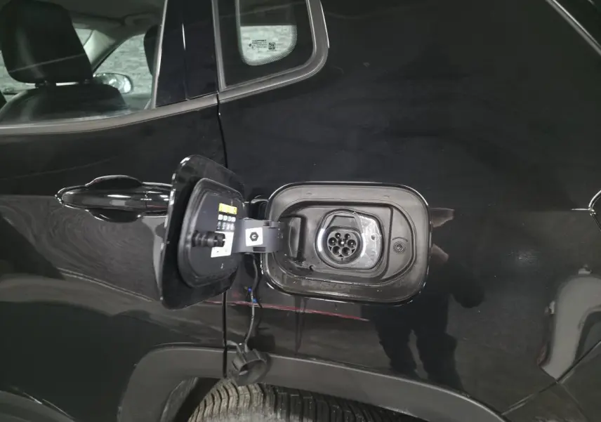 Prise de recharge ouverte côté gauche sur Jeep Compass noir 2024 hybride rechargeable, détail de la trappe et connecteur.