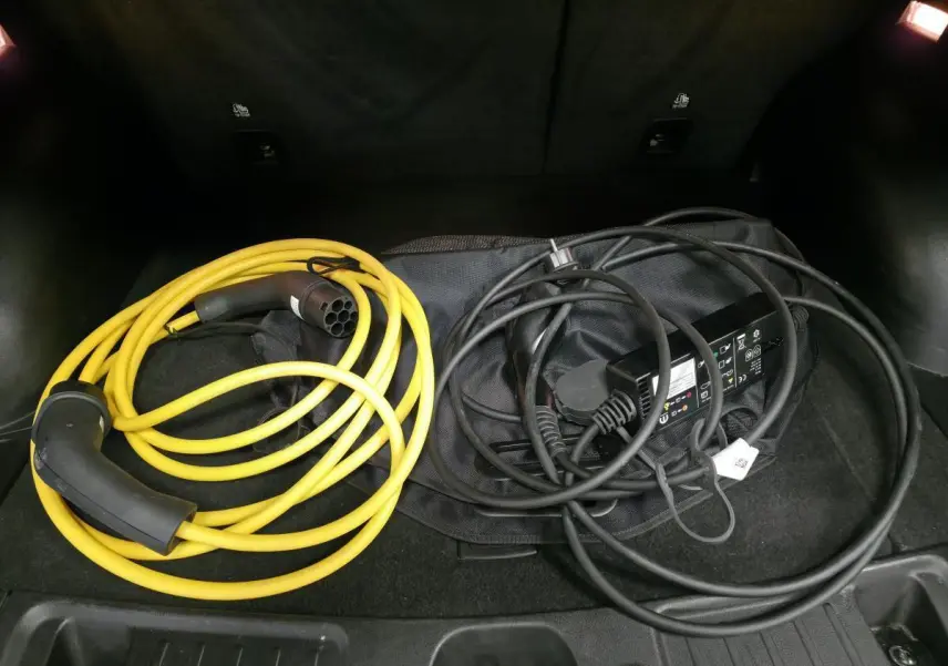 Coffre ouvert d’un Jeep Compass noir 2024 montrant deux câbles de recharge pour hybride rechargeable.