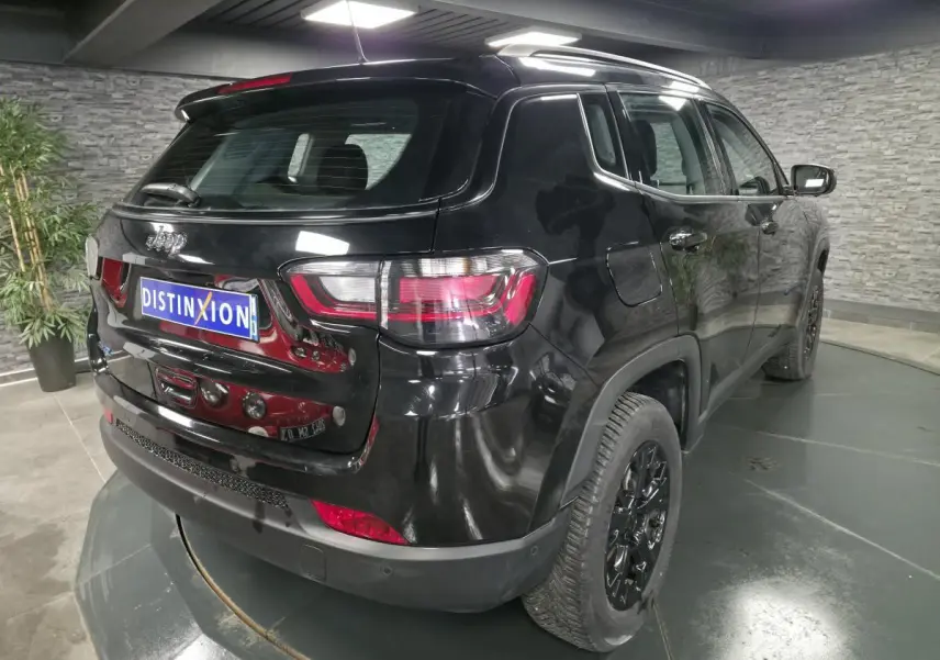 Vue 3/4 arrière droite d'un Jeep Compass noir brillant avec jantes noires et feux arrière LED dans un showroom.