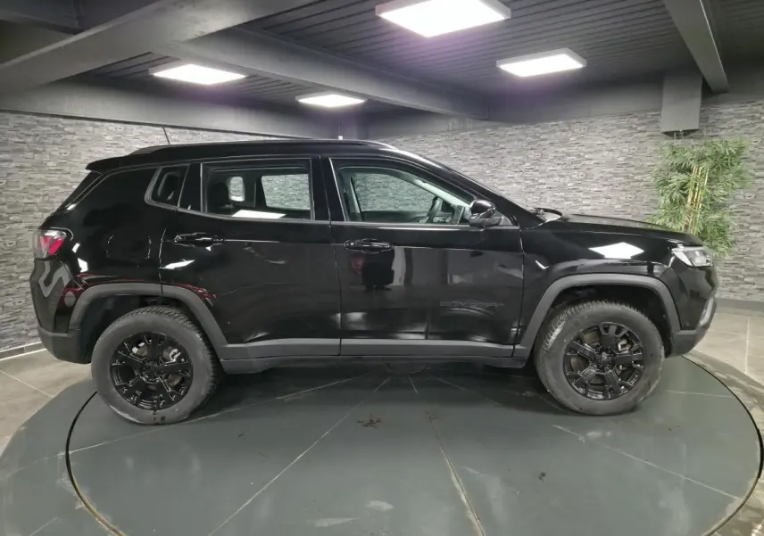 Jeep Compass noir vue de profil côté gauche, avec jantes alliage noires et garde au sol surélevée dans un showroom.