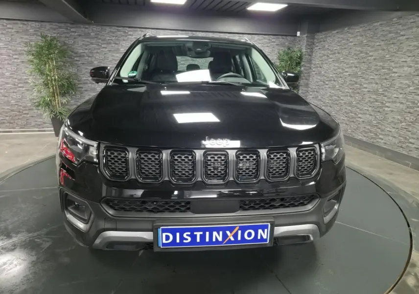Vue avant d'un Jeep Compass noir 2024 avec calandre distinctive et plaque Distinxion en intérieur showroom.