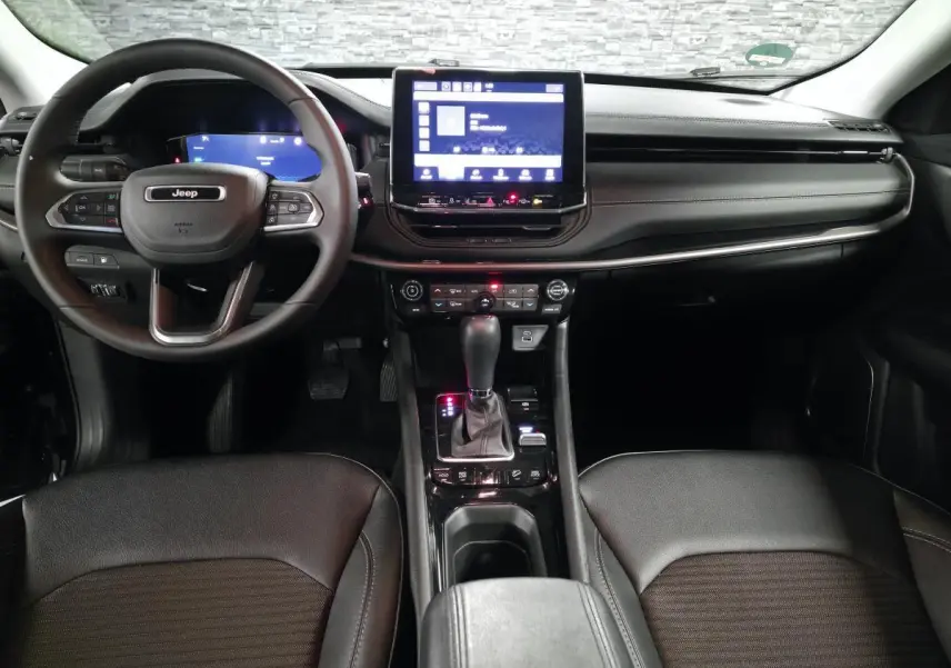 Vue intérieure avant du Jeep Compass 2024 noir, avec tableau de bord numérique et écran tactile central lumineux.