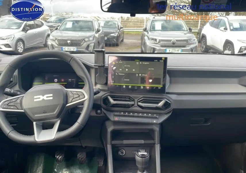 Tableau de bord et volant du Dacia Duster 2026 vert cèdre, vue frontale intérieure avec écran tactile et boîte manuelle.