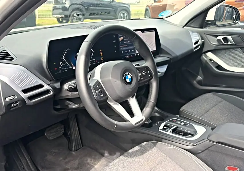 Vue intérieure côté conducteur de la BMW Série 1 120da 2025 avec volant cuir M et écran tactile moderne.