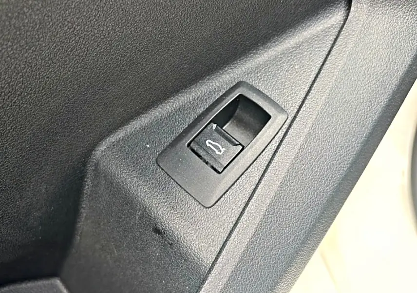 Gros plan sur le bouton d'ouverture du coffre intégré dans le panneau de porte intérieur noir.