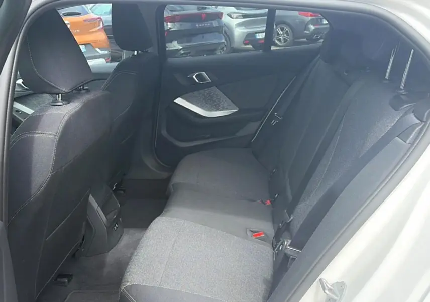 Vue intérieure arrière côté droit de la BMW Série 1 blanche, montrant la banquette tissu gris et la portière ouverte.