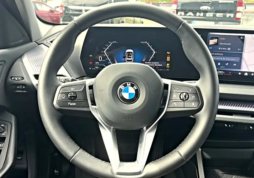 Vue centrée sur le volant cuir noir de la BMW Série 1 120da 2025 avec tableau de bord numérique et écran tactile.