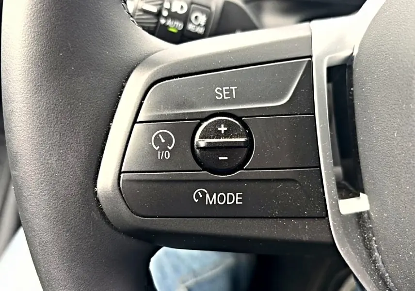 Gros plan sur les commandes de régulateur de vitesse au volant cuir noir d'une BMW Série 1 blanche.
