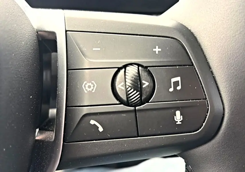 Gros plan sur les commandes noires multifonctions au volant côté gauche de la BMW Série 1 blanche 2025.