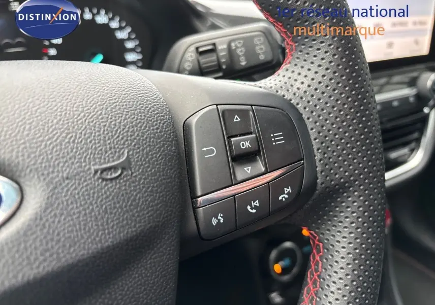 Gros plan sur le volant perforé avec surpiqûres rouges du Ford Puma gris Solar, montrant les commandes multifonctions.