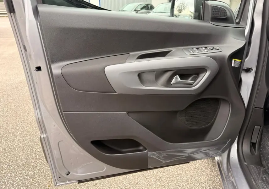 Vue intérieure de la porte avant gauche du Citroën Berlingo gris Artense, avec commandes électriques et haut-parleur intégré.