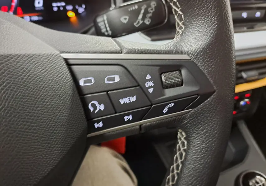 Gros plan sur les commandes du volant en cuir noir de la SEAT IBIZA 2024, avec boutons rétroéclairés et surpiqûres contrastées.