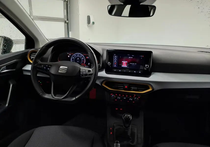 Vue intérieure avant de la SEAT Ibiza 2024 noire, avec tableau de bord numérique, écran tactile et levier de vitesses manuel.