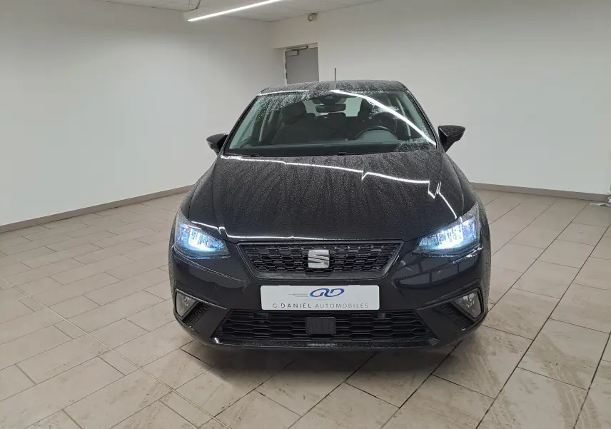 Vue frontale d'une SEAT Ibiza 2024 noir minuit avec projecteurs EcoLED allumés dans un showroom.