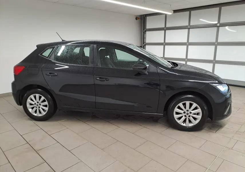 Vue de profil côté droit d'une SEAT Ibiza 2024 noir minuit avec jantes alliage 15'' dans un garage lumineux.