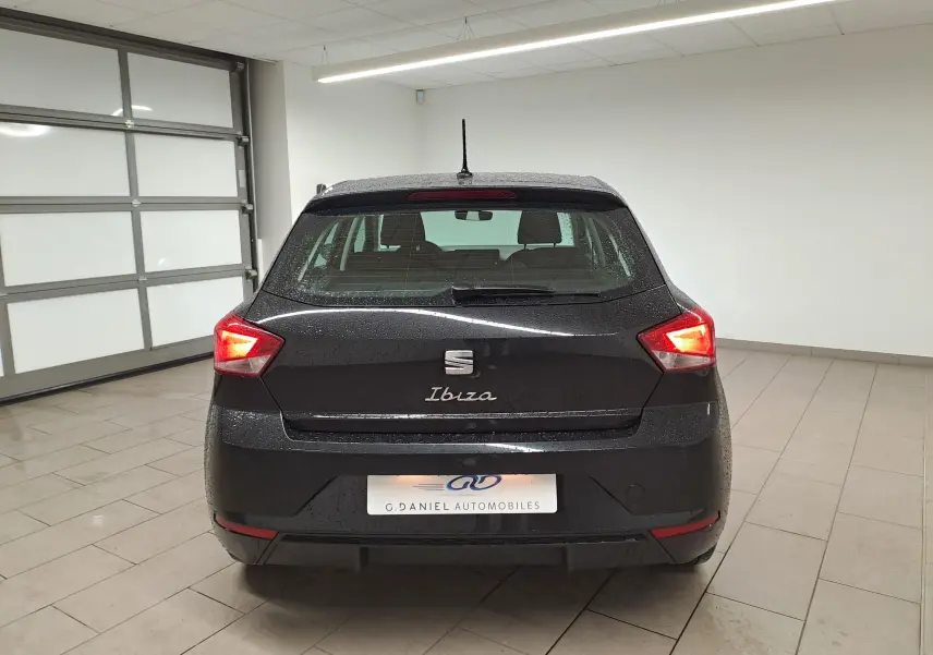 Vue arrière d'une SEAT Ibiza noire minuit 2024 avec feux arrière allumés dans un garage lumineux.