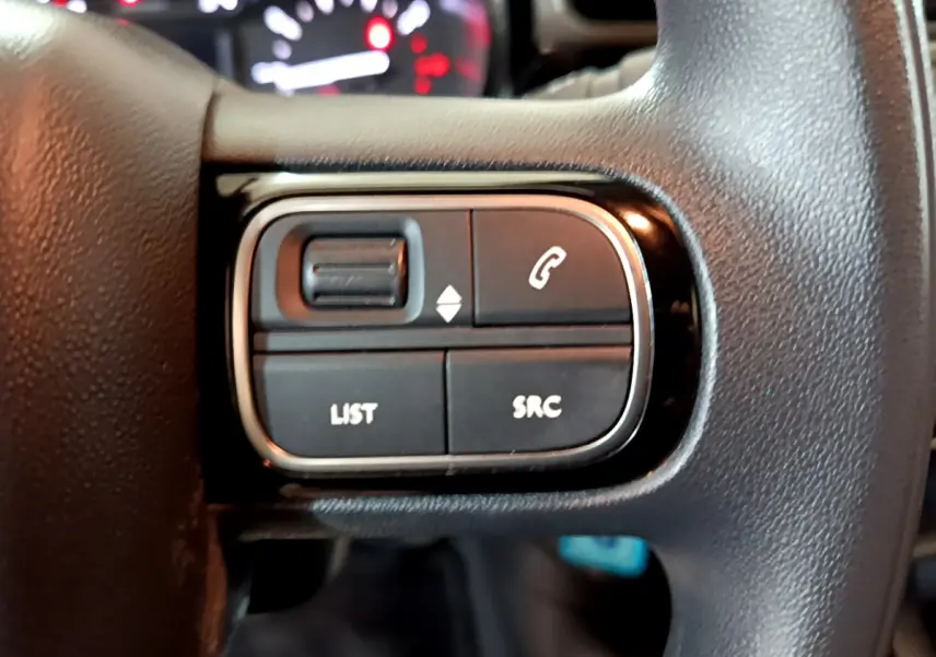 Gros plan sur les commandes noires du volant de la Citroën C3 beige, avec tableau de bord flou en arrière-plan.