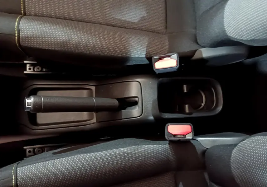 Vue plongeante sur la console centrale noire de la Citroën C3 beige, avec frein à main manuel et ceintures rouges.