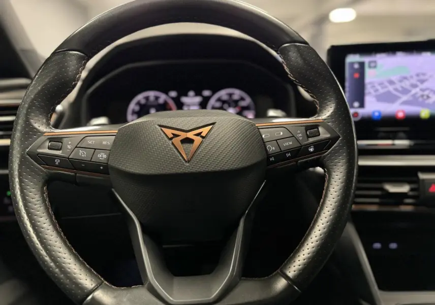 Volant sport noir avec logo CUPRA cuivre au centre, vue frontale sur le tableau de bord digital et écran tactile GPS.