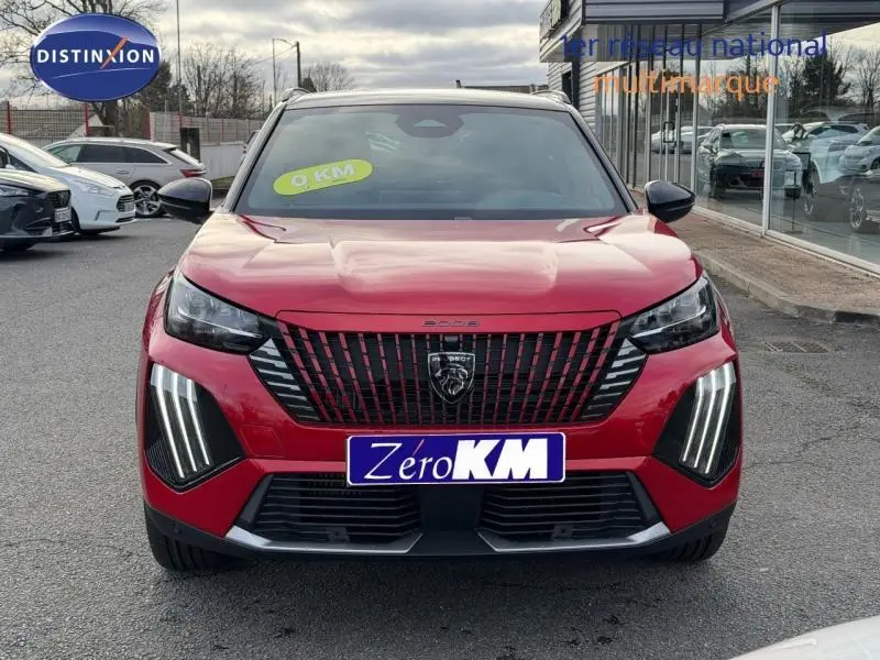Vue frontale d'un Peugeot 2008 rouge avec feux LED verticaux et calandre noire distinctive, en extérieur sur parking.