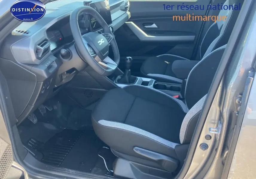 Vue intérieure côté conducteur du Dacia Duster gris schiste 2026, avec volant multifonction et siège tissu noir et gris.