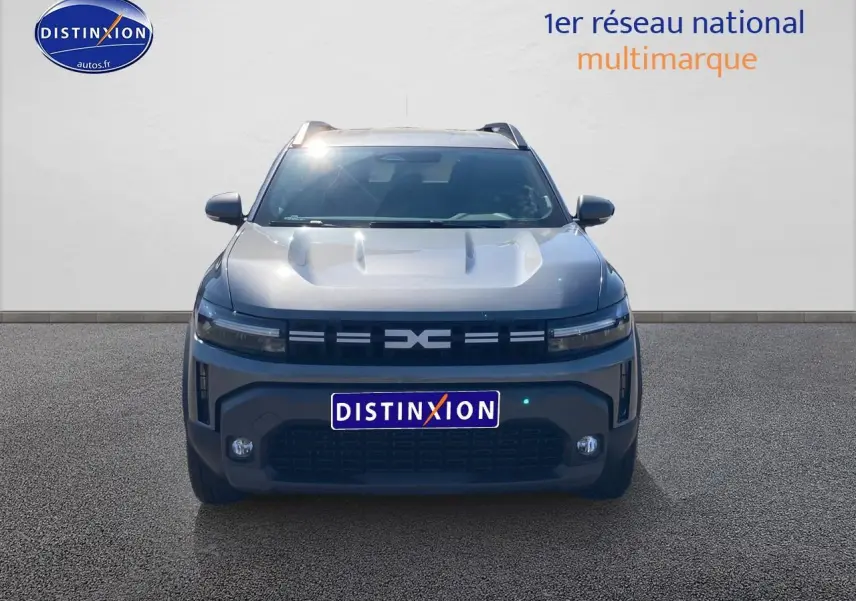 Vue frontale d'un Dacia Duster 2026 gris schiste avec calandre noire et phares LED fins allumés.