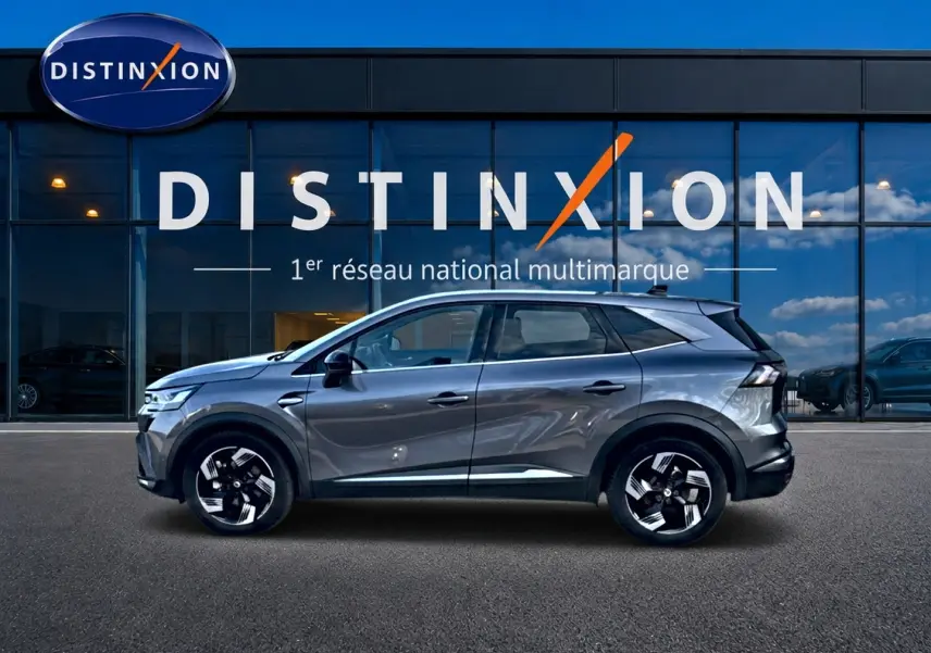 Profil droit d’un Renault Symbioz gris cassiopée 2025 devant une vitrine avec logo Distinxion.