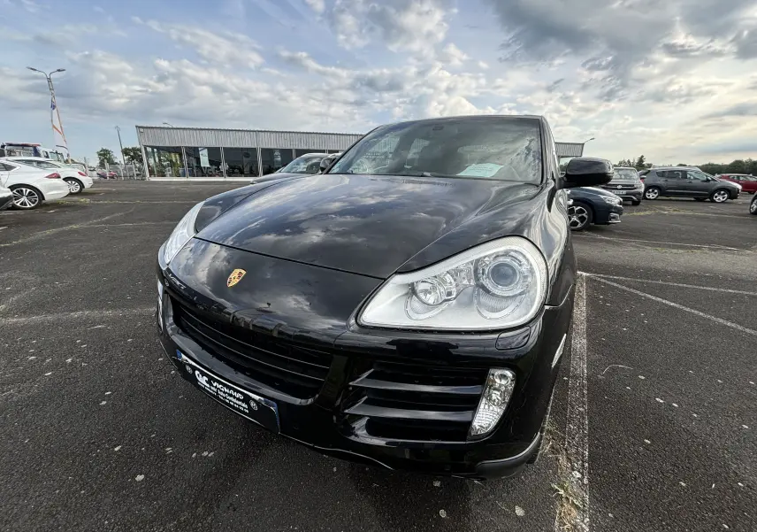 Vue 3/4 avant d'un Porsche Cayenne S noir brillant, mettant en valeur ses phares distinctifs et son logo Porsche sur le capot.