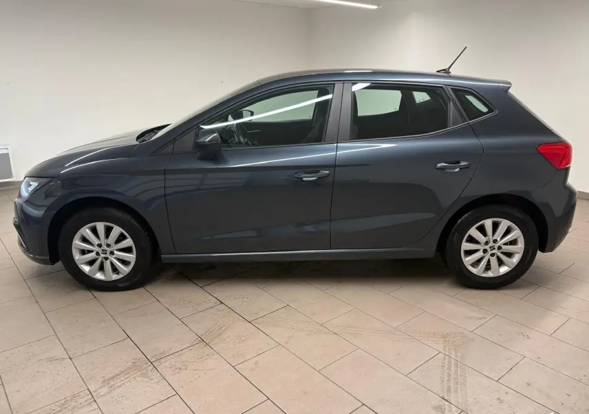 Vue de profil côté gauche d'une SEAT Ibiza 2024 gris magnétique, compacte et élégante, stationnée en intérieur.