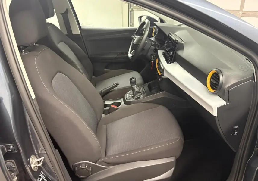 Intérieur avant droit de la SEAT Ibiza 2024 gris magnétique, avec volant, boîte manuelle et aérateurs jaunes distinctifs.