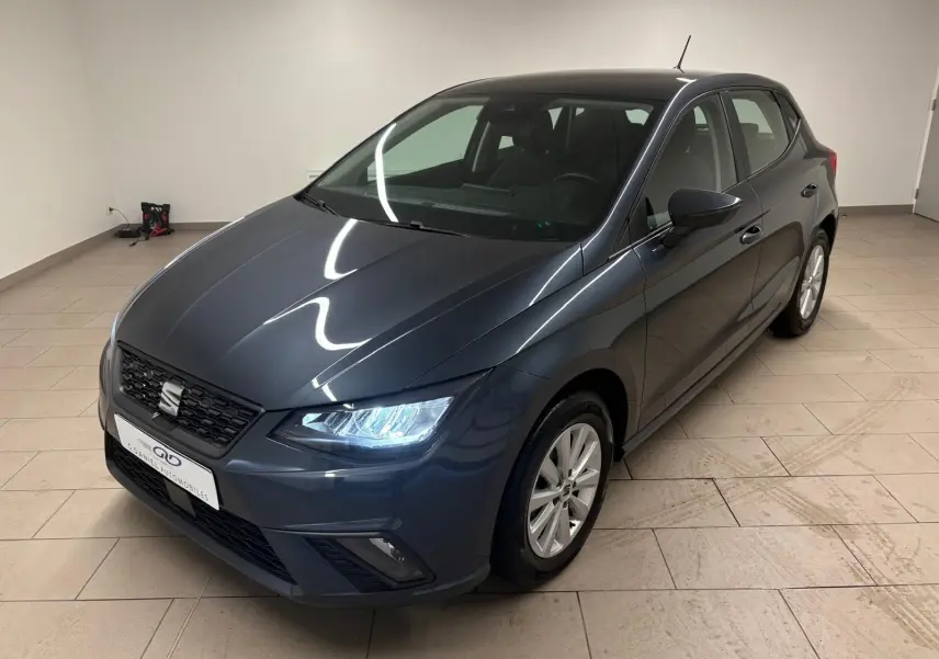 SEAT Ibiza 2024 gris magnétique vue 3/4 avant droit avec phares allumés dans un intérieur neutre.