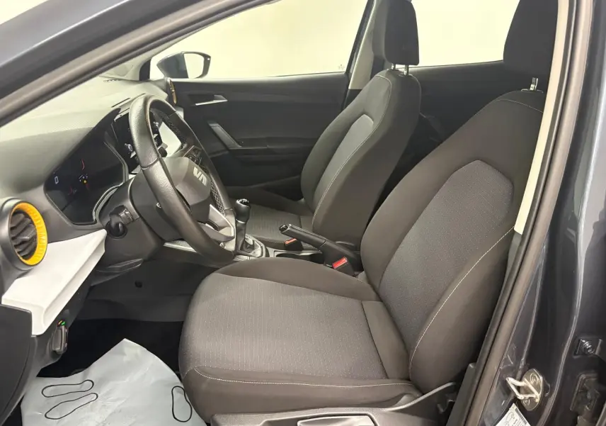 Intérieur avant droit de la SEAT Ibiza 2024 gris magnétique, montrant sièges tissu, volant et levier de vitesses manuel.