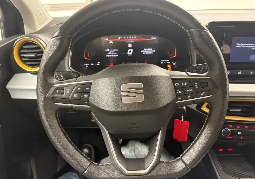 Vue intérieure centrée sur le volant cuir de la SEAT Ibiza 2024 gris magnétique avec tableau de bord numérique et aérateurs jaunes.