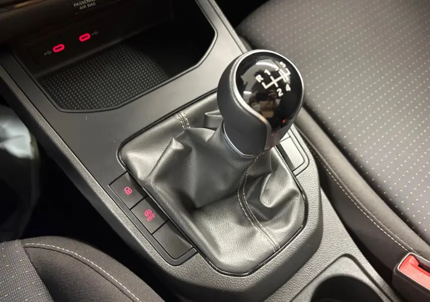 Gros plan sur le levier de vitesse manuel noir de la SEAT Ibiza gris magnétique 2024, avec console centrale et siège tissu visible.