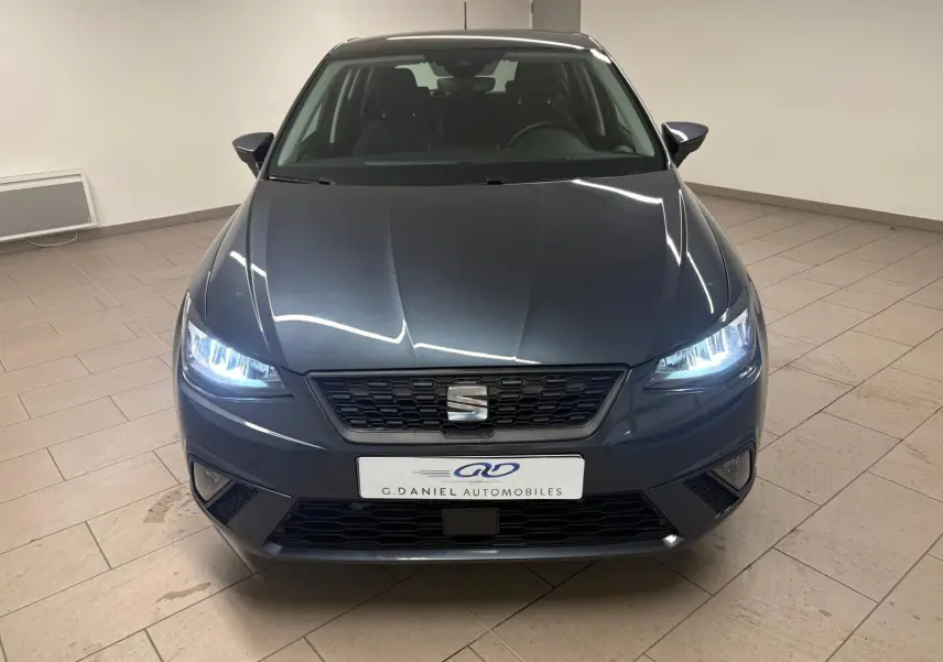 Vue frontale d'une SEAT Ibiza 2024 gris magnétique avec phares allumés dans un showroom intérieur.