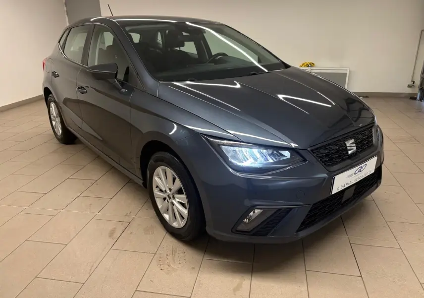 Vue 3/4 avant d'une SEAT Ibiza gris magnétique 2024 avec phares allumés dans un garage intérieur.