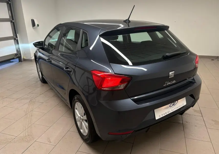 SEAT Ibiza 2024 gris magnétique vue 3/4 arrière droit en intérieur avec feux arrière rouges visibles.
