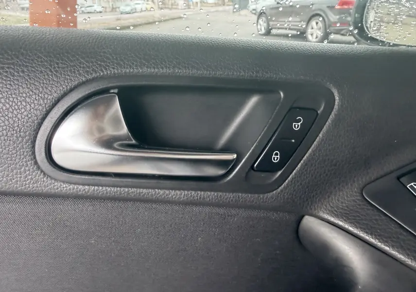 Poignée intérieure de porte côté gauche en plastique noir avec boutons de verrouillage sur Volkswagen Tiguan 2010.