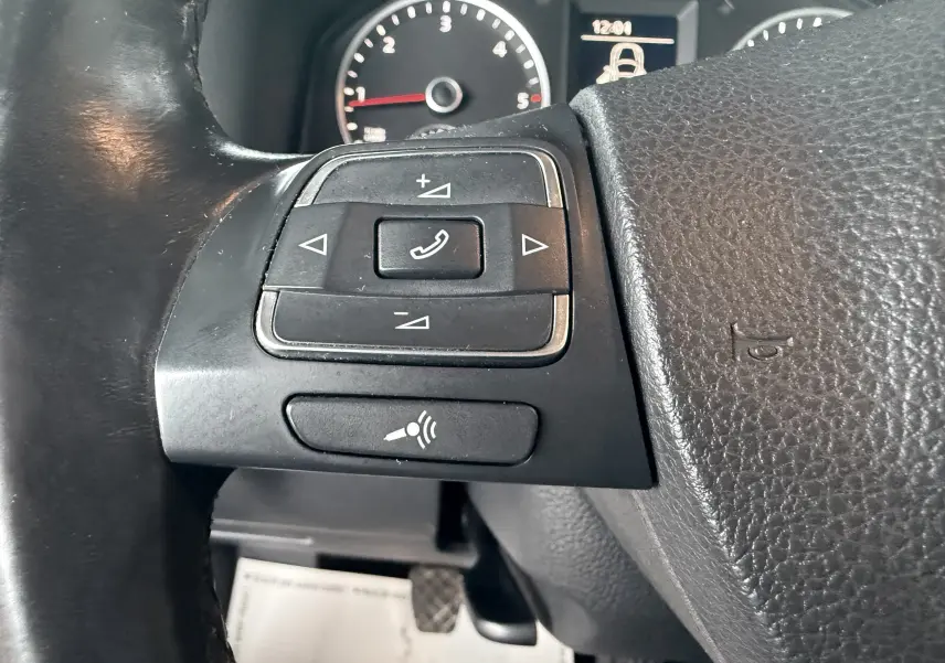 Gros plan sur les commandes au volant noir du Volkswagen Tiguan 2010, avec compteur et affichage digital en arrière-plan.