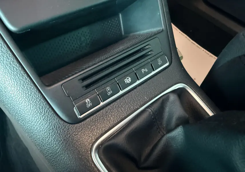 Gros plan sur la console centrale du Volkswagen Tiguan blanc de 2010, avec levier de vitesse manuel et boutons de contrôle.