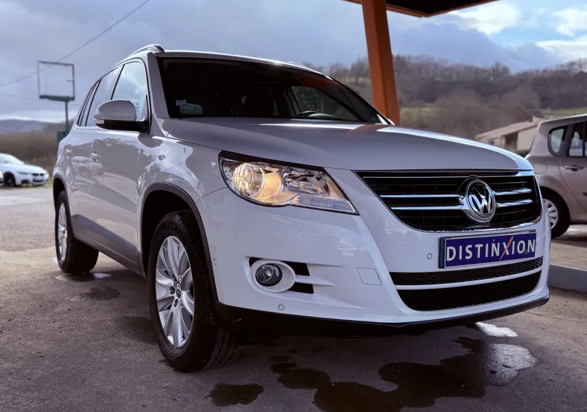 Volkswagen Tiguan blanc vue 3/4 avant gauche avec phares allumés sous un abri en extérieur.