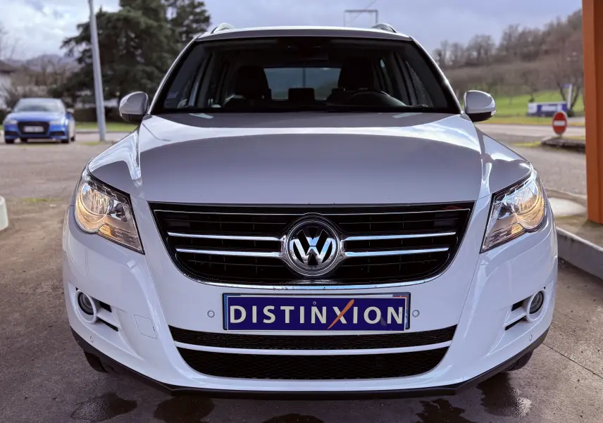 Vue frontale d'un Volkswagen Tiguan blanc de 2010 avec calandre noire et plaque Distinxion visible.