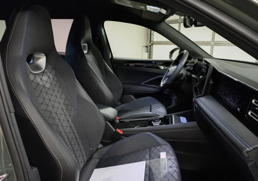 Vue intérieure côté conducteur du Volkswagen Tiguan 2025, sièges sport noirs avec surpiqûres bleues et tableau de bord digital.