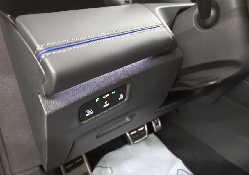 Détail du tableau de bord côté conducteur avec commandes d’éclairage et surpiqûres bleues sur cuir noir.