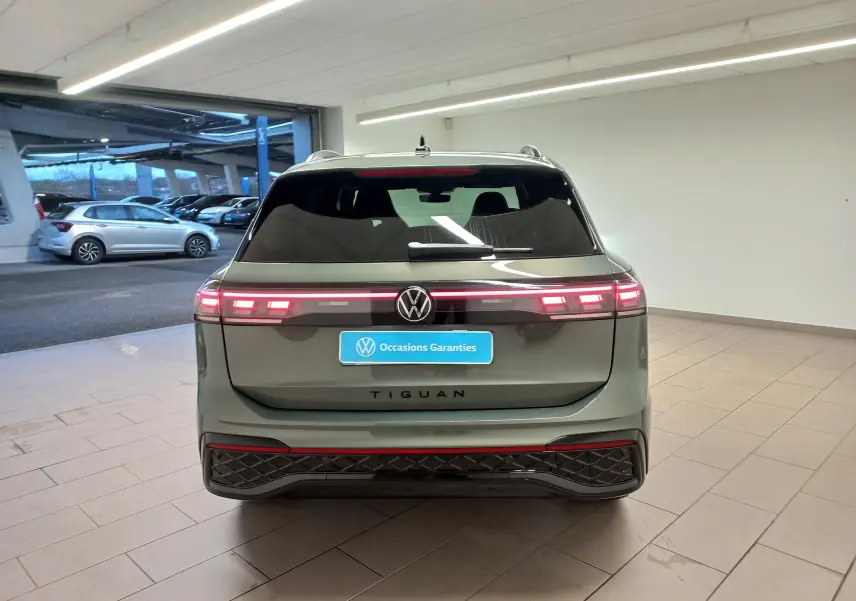 Vue arrière du Volkswagen Tiguan 2025 vert Cipressino avec feux LED allumés dans un garage intérieur.