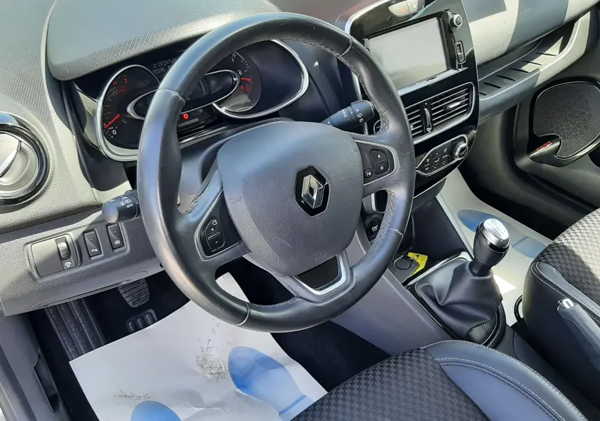 Vue intérieure de face du poste de conduite de la Renault Clio IV gris titanium, volant multifonction et levier de vitesses manuel visibles.