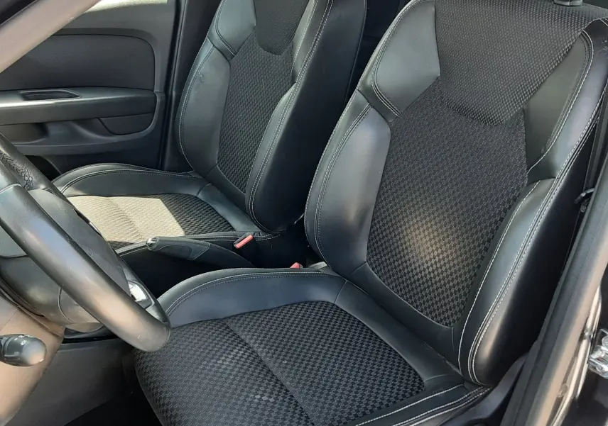 Vue intérieure côté conducteur de la Renault Clio IV 0.9 TCE 90 Intens, sièges noirs en cuir et tissu avec surpiqûres blanches.