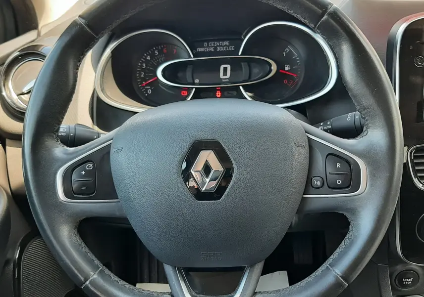 Vue rapprochée du volant en cuir noir avec logo Renault, tableau de bord et commandes visibles à l'intérieur d'une Clio IV.