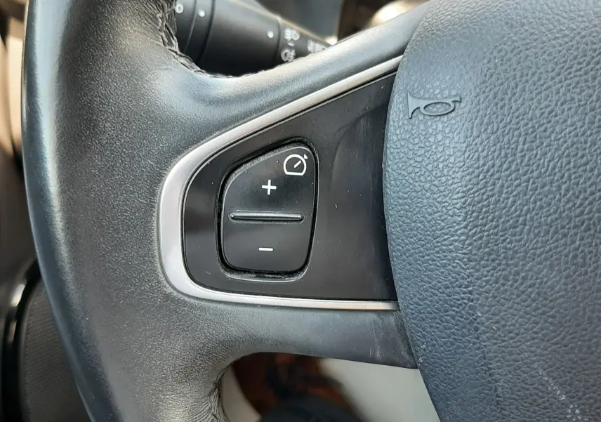 Gros plan sur les commandes de régulateur de vitesse à gauche du volant noir de la Renault Clio IV gris titanium.