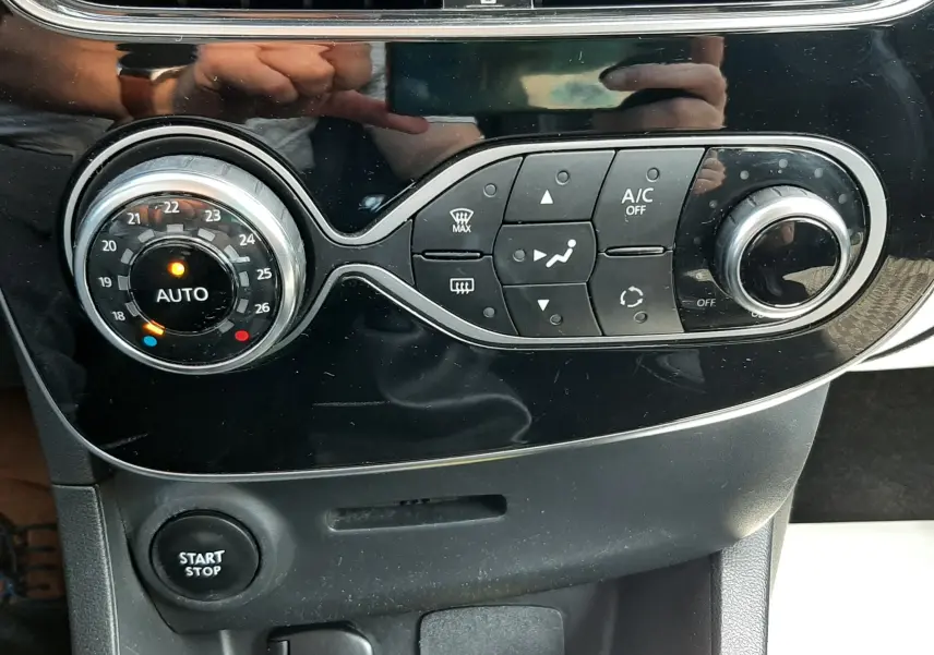 Vue rapprochée de la console centrale noire de la Renault Clio IV gris titanium, montrant les commandes de climatisation et le bouton start/stop.